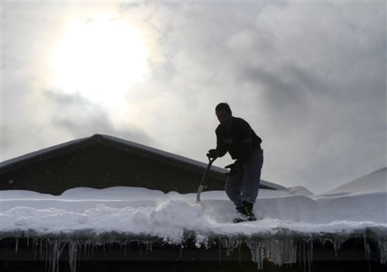 The sun begins to break through the clouds as Anesti Karathanasis works to shovel snow from the latest storm off the roof of his restaurant on Friday in Concord, N.H.